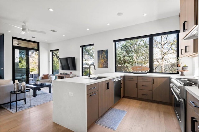 kitchen with light countertops, appliances with stainless steel finishes, open floor plan, a sink, and a peninsula