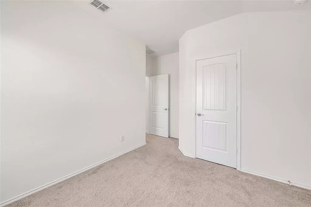 unfurnished bedroom featuring lofted ceiling, baseboards, visible vents, and light colored carpet