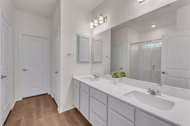 full bath with double vanity, a stall shower, a sink, and wood finished floors