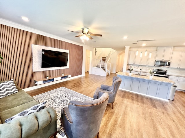 living area featuring ceiling fan, stairway, light wood-type flooring, and crown molding