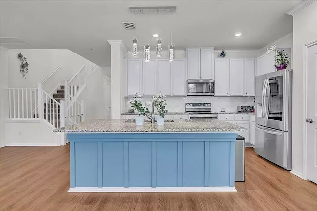 kitchen with appliances with stainless steel finishes, a center island with sink, visible vents, and white cabinetry