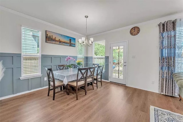 dining room featuring ornamental molding, a notable chandelier, a decorative wall, and wood finished floors