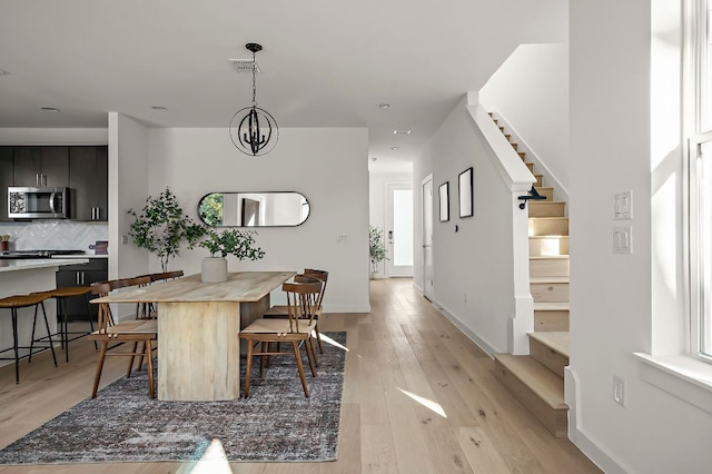 dining area with visible vents, baseboards, stairway, an inviting chandelier, and light wood-style floors