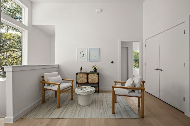 sitting room featuring baseboards, a high ceiling, wood finished floors, and a healthy amount of sunlight