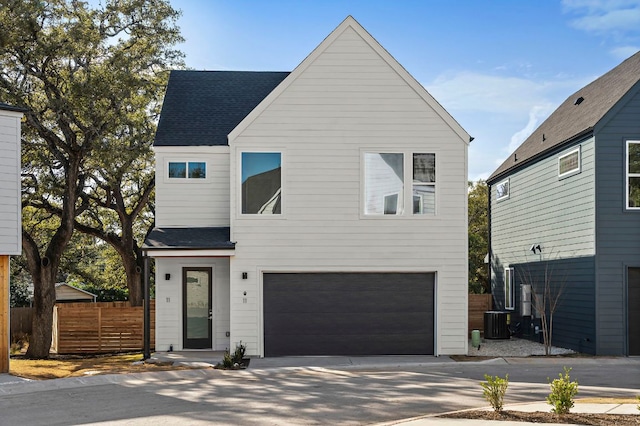 modern home featuring an attached garage, fence, central AC unit, and roof with shingles