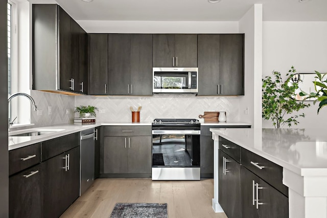 kitchen with stainless steel appliances, light countertops, a sink, and light wood finished floors