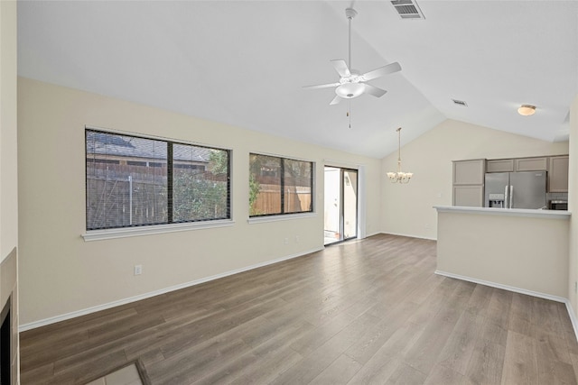 unfurnished living room featuring lofted ceiling, visible vents, wood finished floors, baseboards, and ceiling fan with notable chandelier