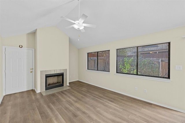 unfurnished living room featuring a ceiling fan, wood finished floors, a tiled fireplace, baseboards, and lofted ceiling