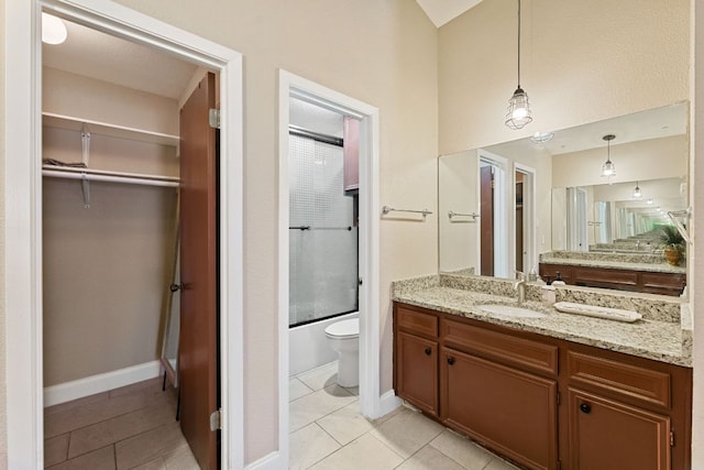 bathroom featuring a walk in closet, toilet, vanity, tile patterned flooring, and baseboards