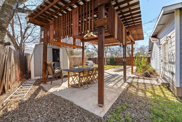 view of patio featuring an outbuilding, outdoor dining area, a fenced backyard, and a storage unit