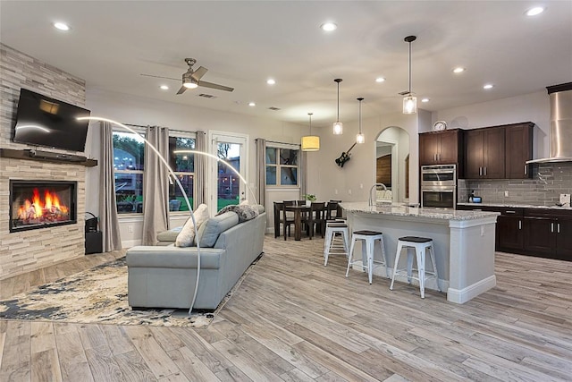 kitchen with a breakfast bar, decorative backsplash, double oven, open floor plan, and wall chimney exhaust hood