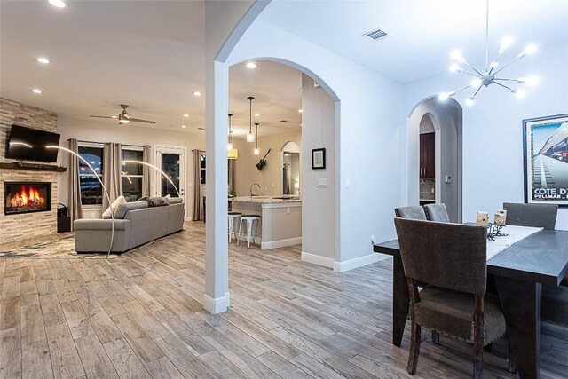 5608 Arroyo Rd, Austin, TX 78734 - dining area featuring light wood finished floors, a ceiling fan, a stone fireplace, recessed lighting, and arched walkways
