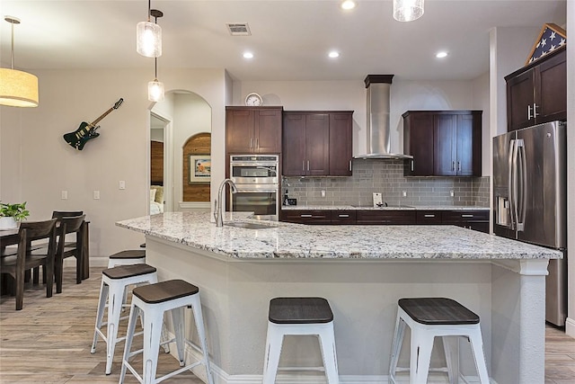 5608 Arroyo Rd, Austin, TX 78734 - kitchen with stainless steel appliances, wall chimney range hood, light wood-style flooring, dark brown cabinets, and a breakfast bar area
