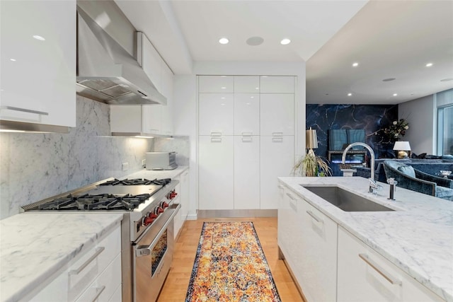 kitchen featuring high end stainless steel range, white cabinetry, a sink, wall chimney range hood, and modern cabinets