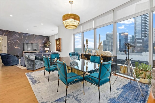 dining space with a chandelier, recessed lighting, an accent wall, wood finished floors, and a view of city