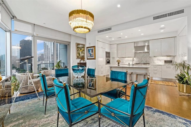 dining area featuring light wood finished floors, visible vents, a chandelier, and a city view