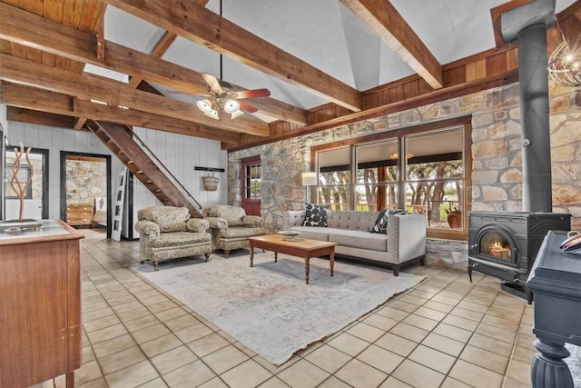 living area with vaulted ceiling with beams, light tile patterned flooring, a ceiling fan, stairway, and a wood stove