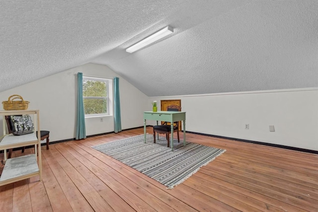 interior space featuring light wood-style floors, baseboards, vaulted ceiling, and a textured ceiling