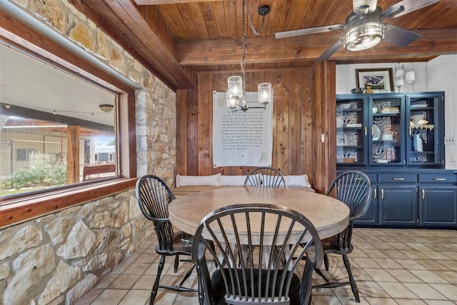 dining area with wood ceiling, beamed ceiling, ceiling fan with notable chandelier, wood walls, and light tile patterned flooring