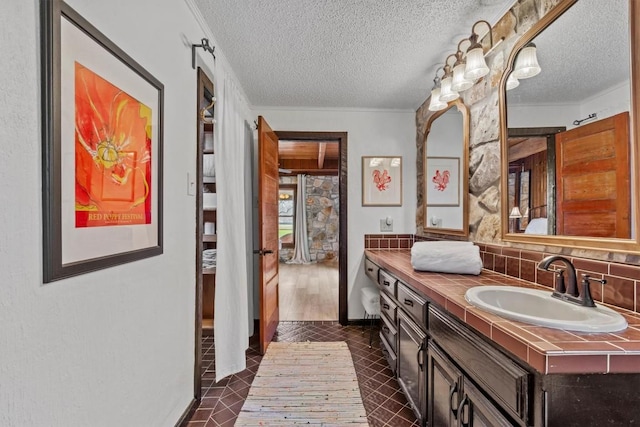 bathroom with a textured ceiling, crown molding, vanity, and decorative backsplash