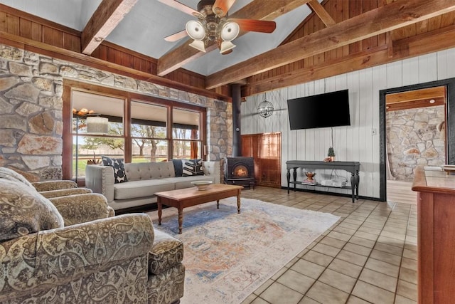 tiled living room with wooden walls, a ceiling fan, a towering ceiling, a wood stove, and beam ceiling