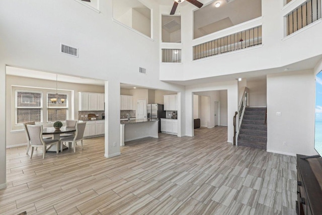 unfurnished living room with ceiling fan with notable chandelier, wood finish floors, stairway, and visible vents