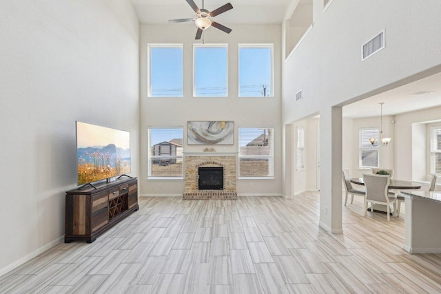 living area with light wood-style flooring, ceiling fan with notable chandelier, visible vents, baseboards, and a brick fireplace