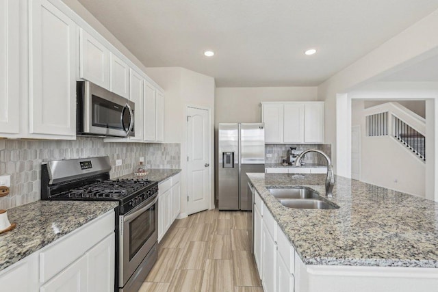 kitchen featuring white cabinets, stainless steel appliances, a sink, and an island with sink