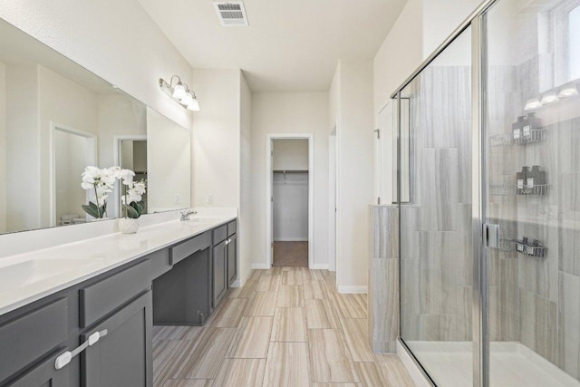 bathroom featuring a sink, visible vents, a spacious closet, a shower stall, and double vanity