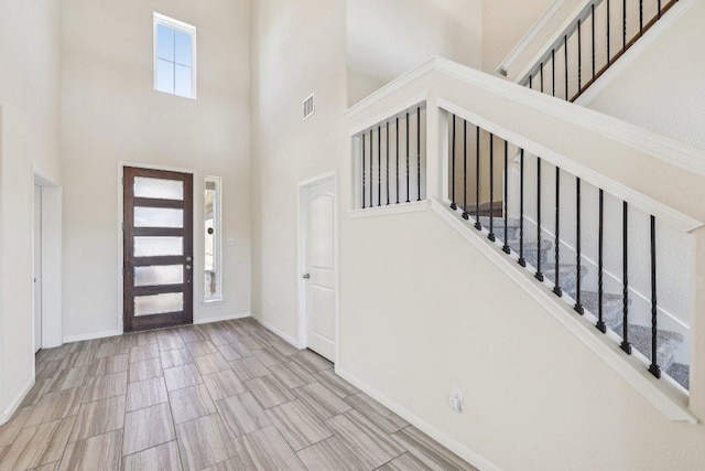 entrance foyer with visible vents, a towering ceiling, stairway, wood tiled floor, and baseboards