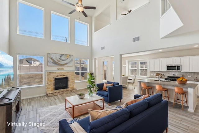 20417 Whimbrel Ct, Pflugerville, TX 78660 - living area featuring ceiling fan, a high ceiling, light wood finished floors, a brick fireplace, and baseboards