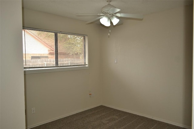 empty room with a ceiling fan, dark carpet, and baseboards