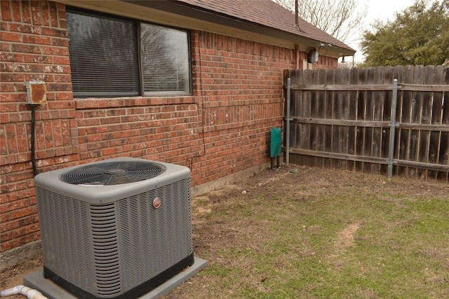 view of side of home with central air condition unit, a shingled roof, fence, and brick siding