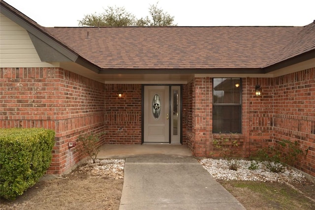 property entrance featuring brick siding and roof with shingles