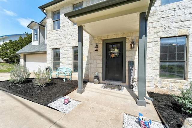 entrance to property featuring a garage, stone siding, and a shingled roof