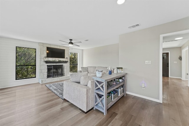 living area with a fireplace, wood finished floors, a ceiling fan, visible vents, and baseboards