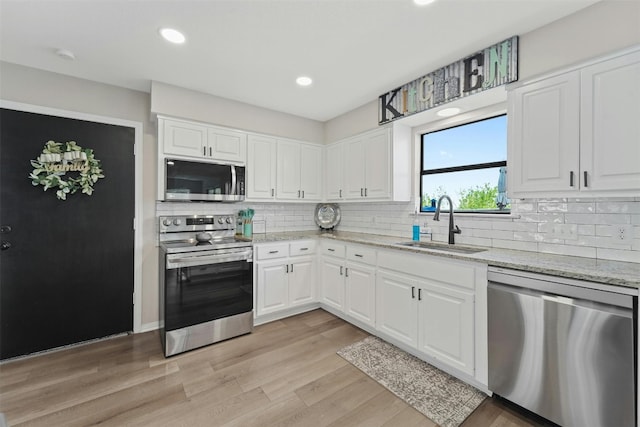 kitchen featuring light wood-style flooring, stainless steel appliances, a sink, white cabinets, and light stone countertops