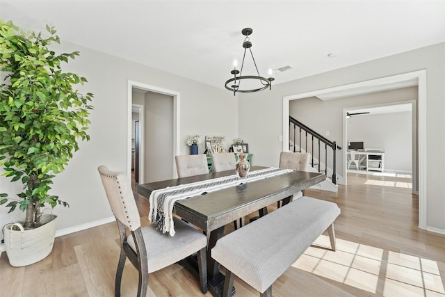 dining space with light wood finished floors, visible vents, stairs, and a chandelier