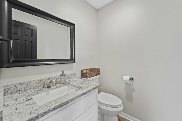 half bathroom with vanity, toilet, and baseboards