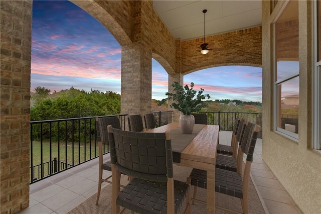 patio terrace at dusk featuring a balcony, ceiling fan, and outdoor dining space