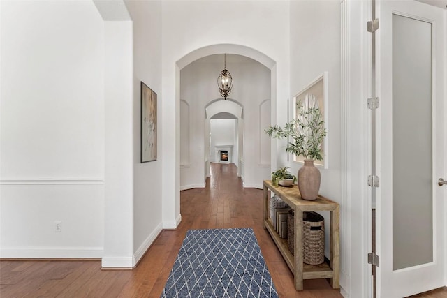 corridor with arched walkways, wood finished floors, and baseboards