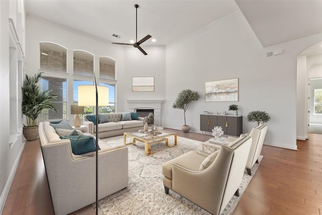 living room with visible vents, arched walkways, a towering ceiling, wood finished floors, and a fireplace