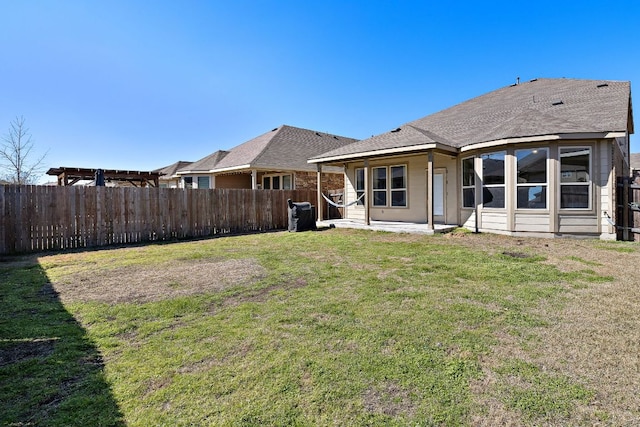 back of property with a fenced backyard, a shingled roof, a lawn, and a patio