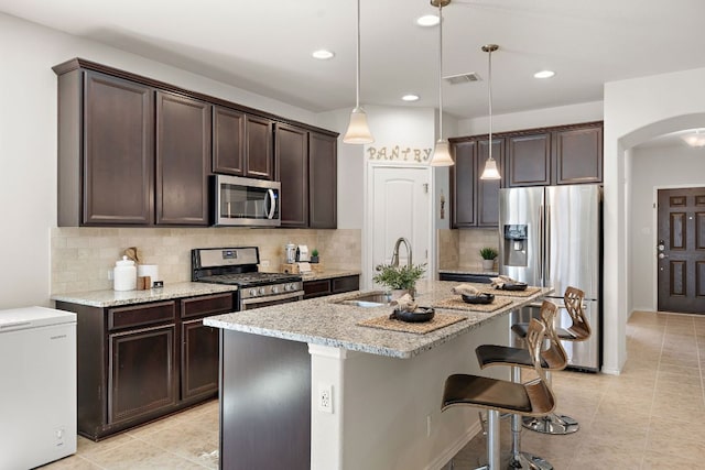 kitchen featuring arched walkways, visible vents, appliances with stainless steel finishes, dark brown cabinets, and light stone countertops