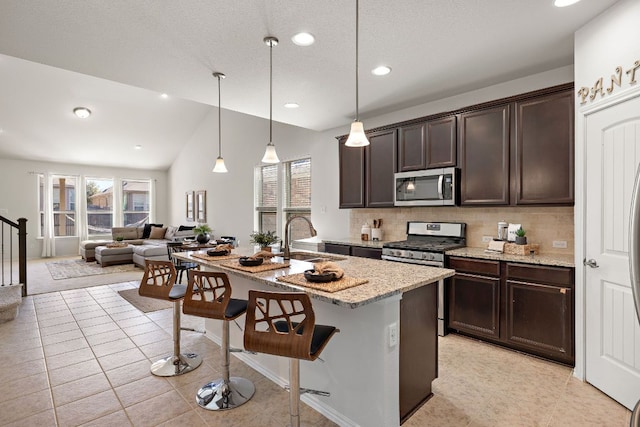 kitchen featuring appliances with stainless steel finishes, a healthy amount of sunlight, a sink, dark brown cabinetry, and a kitchen bar