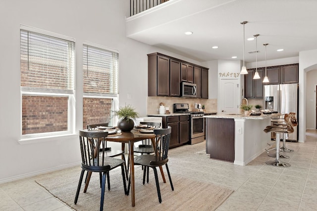 kitchen featuring tasteful backsplash, stainless steel appliances, dark brown cabinets, a kitchen bar, and a sink