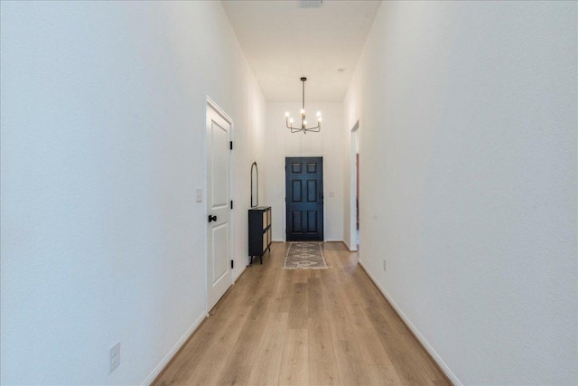 corridor with baseboards, a notable chandelier, a high ceiling, and light wood finished floors