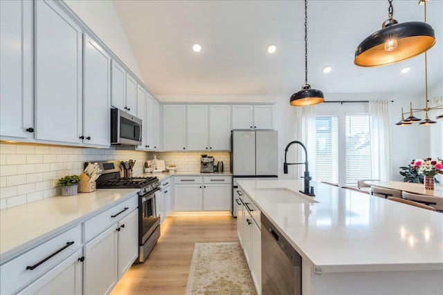 kitchen with a sink, hanging light fixtures, appliances with stainless steel finishes, tasteful backsplash, and light wood-type flooring