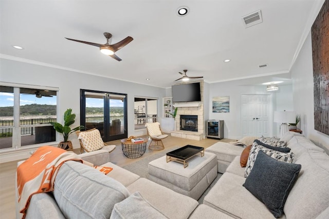 living room featuring crown molding, visible vents, ceiling fan, a stone fireplace, and wood finished floors