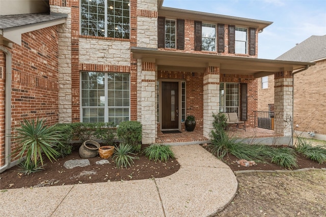 entrance to property featuring stone siding, covered porch, and brick siding